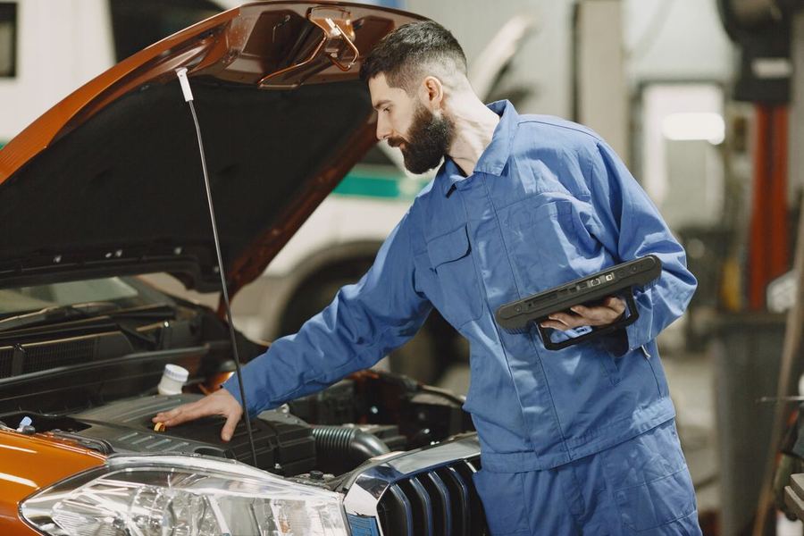 Mechanic in blue coveralls checking an engine bay with a tablet